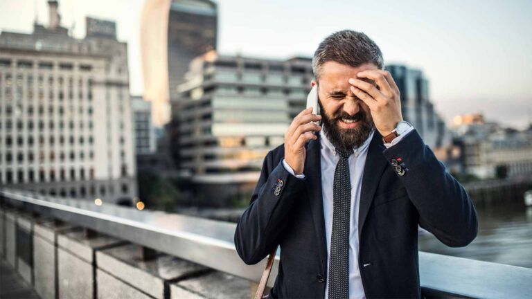 A man in a suit stands on a city bridge, stressed as he handles work calls about commercial printing Spokane needs. With buildings in the background, he contemplates solutions for urgent bulk newsletter printing.